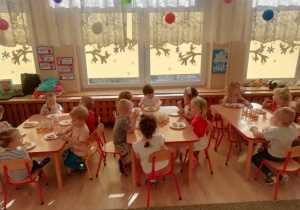 Grupa dzieci siedzi przy stolikach i je pizzę