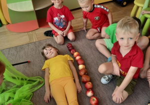 Dzieci mierzą wzrost Martynki ilością jabłek