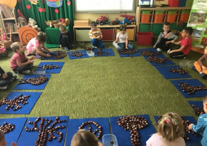 Dzieci układają na dywanikach drzewa z kasztanów