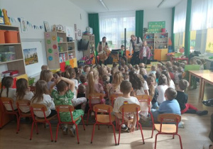 Dzieci siedzą na krzesełkach i słuchają koncertu