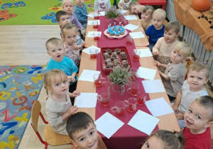 Dzieci siedzą przy stole z przekąskami.