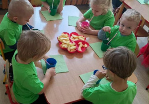 Dzieci piją sok jabłkowy przy stoliku.