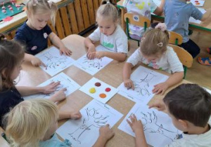 Dzieci malują palcami i farbami jesienne drzewo.