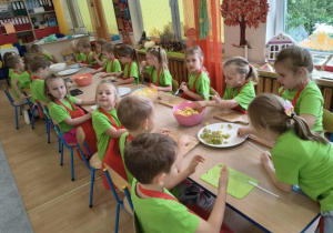 Dzieci kroją składniki na sałatkę przy stoliku.