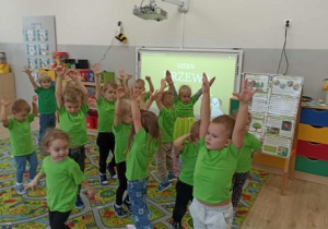 Dzieci chodzą po dywanie z rękami uniesionymi ku górze.