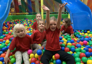 Dzieci siedzą w basenie z kulkami.