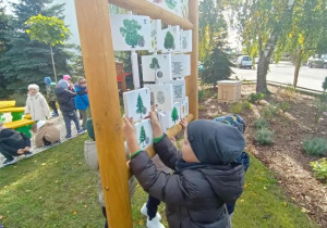 Maks ogląda tablicę dydaktyczną "Co ze mnie wyrośnie" z elementami manipulacyjnymi.