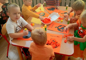 Dzieci wyklejają dynię kawałkami bibuły.