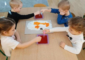 Dzieci wykonują prace plastyczną z użyciem zakraplaczy.