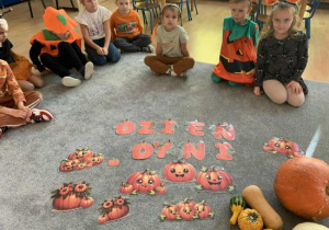 Dzieci siedzą na dywanie z napisem Dzień Dyni.