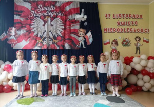Dziewczynki z grupy Pszczółek na tle dekoracji z okazji Święta Niepodległości.