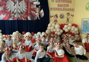 Dzieci siedzą na tle dekoracji z okazji Święta Niepodległości.