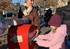 Dziewczynka wrzuca list do św. Mikołaja do czerwonej skrzynki pocztowej.