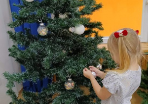 Dziewczynka zawiesza srebrną bombkę na choince.