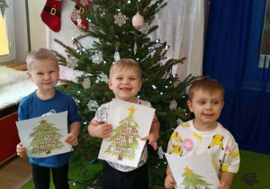 Chłopcy pokazują wykonane przez siebie prace plastyczne.