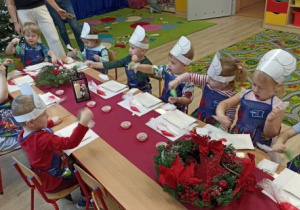 Dzieci dekorują pierniki przy świątecznym stole.