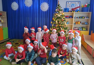 Dzieci z grupy Motylków pozują do zdjęcia w mikołajowych czapkach.