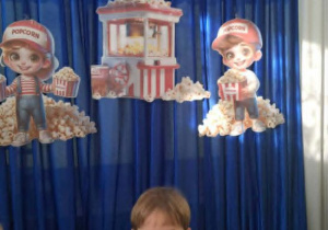 Chłopiec z grupy Motylków stoi z paczką popcornu na tle dekoracji.