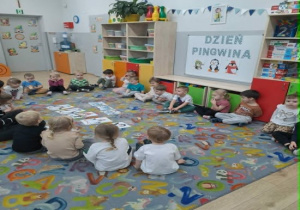 Dzieci siedzą w kole na dywanie i oglądają zdjęcia różnych rodzajów pingwinów