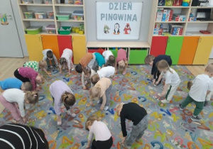Dzieci chodzą pochylone po dywanie i naśladują pingwiny