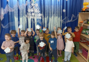 Dzieci śpiewają piosenkę o płatkach śniegu machając papierowymi płatkami śniegu