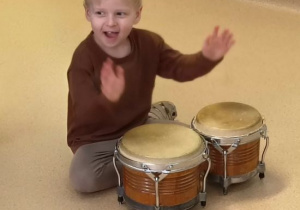 Chłopiec siedzi i gra na bębnach.