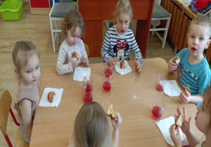 Dzieci siedzą przy stoliku i jedzą pączki.