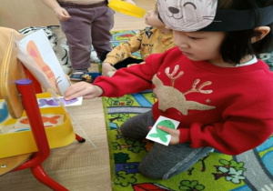 Dziewczynka karmi papierowego kota papierowymi rybami.