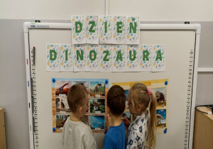 Dzieci oglądają wystawę zdjęć dinozaurów.