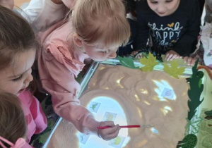 Dzieci przy pomocy pędzelka odkrywają dinozaury.