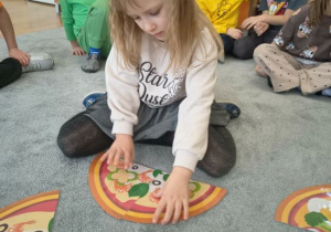 Dziewczynka układa puzzle z pizzą.