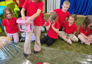 Dziewczynka rzuca klocki na folię, pod którą jest inne dziecko.