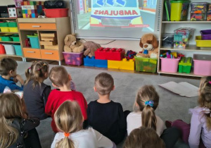 Dzieci oglądają film edukacyjny o numerze alarmowym.