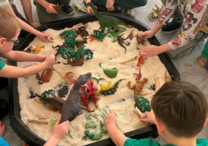 Chłopcy bawią się dinozaurami na tacy z ryżem