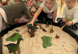 Dziewczynki bawią się dinozaurami na tacy z ryżem