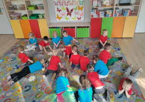 Dzieci naśladują motylki i na pauzę w muzyce siadają na kwiatach rozłożonych na dywanie.