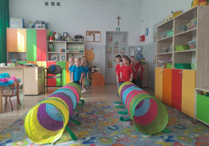 Dziecistoją w dwóch rzędach przed kolorowymi tunelami gąsienicowymi.