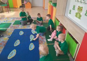 03 Dzieci siedzą na dywanie dziewczynka dopasowuje żaby do talerzy z odpowiednią ilością przysmaków według liczby kropek na żabie.