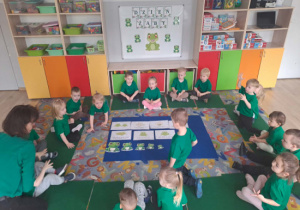 Dzieci siedzą w kole na dywanie chłopiec na środku układa żaby od największej do najmniejszej.