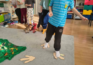 Szymon idzie po tekturowych śladach dinozaura.