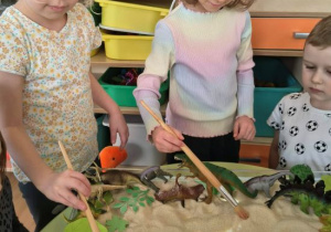 Dziewczynki odkopują szkielety dinozaurów.