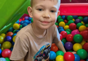 Aleks siedzi w basenie z piłkami.