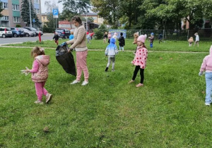 Dzieci wraz z Panią sprzątają najbliższą okolicę przedszkola.