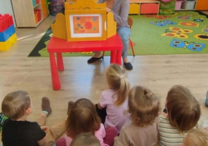 Pani za pomocą teatrzyku kamishibai czyta dzieciom bajke.