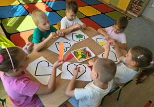 Dzieci wyklejają kontur serca skrawkami kolorowego papieru.